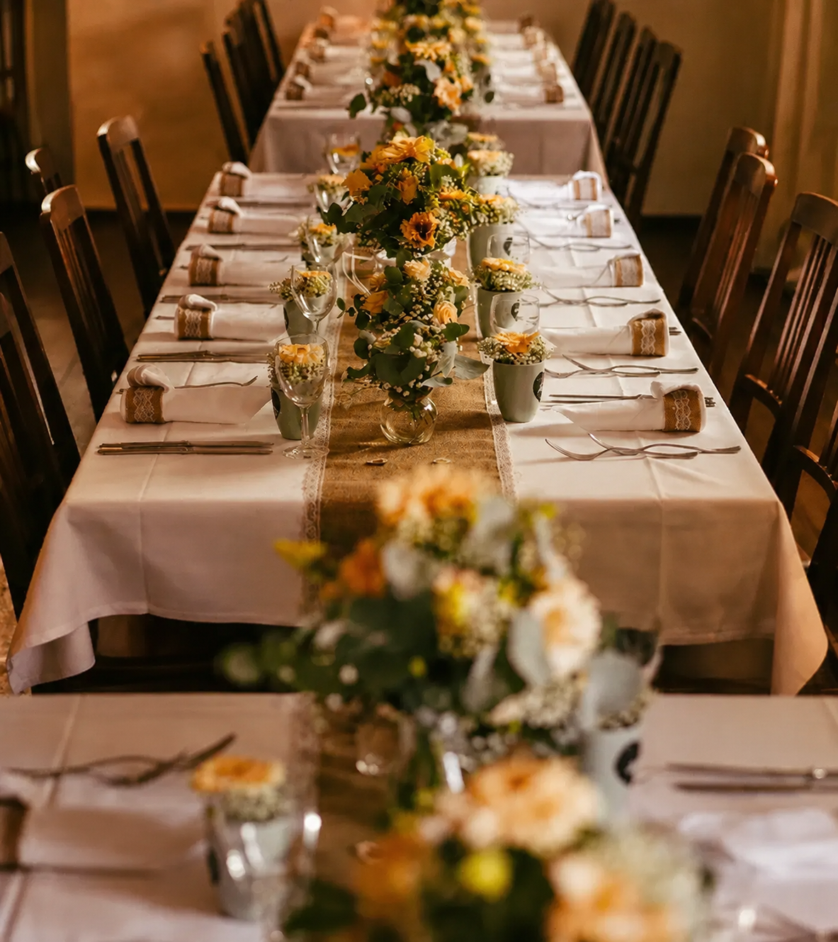 Lange rustikale Hochzeitstafel mit vielen kleinen Gefäßen, gelben Rosen, Schleierkraut und Eukalyptus auf Jutläufer