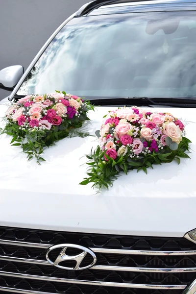 Zweiteiliger Autoschmuck in Rosa und Creme aus Rosen, Nelken und Schleierkraut auf der weißen Motorhaube eines Hochzeitsautos